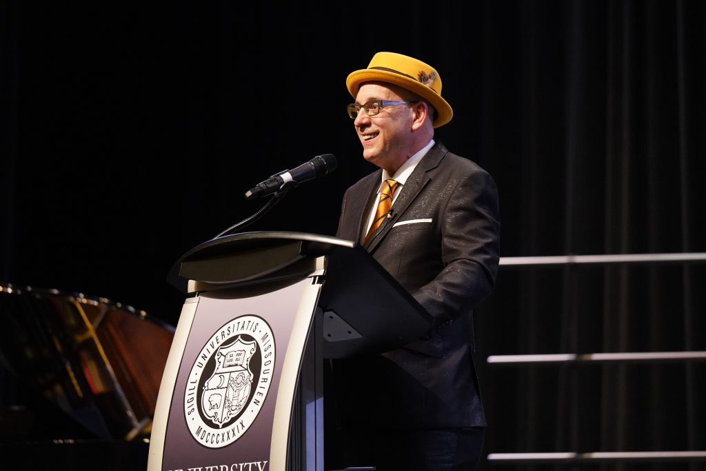 Cal Fussman standing at a podium and speaking.
