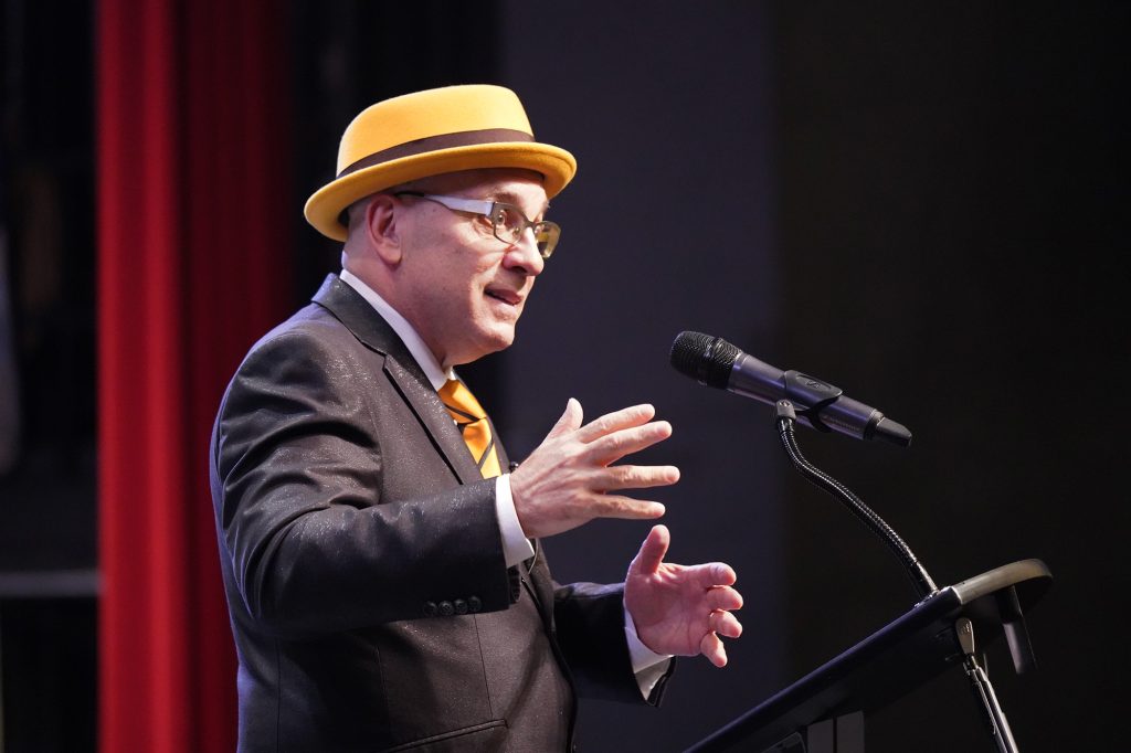 Cal Fussman standing at a podium and speaking.